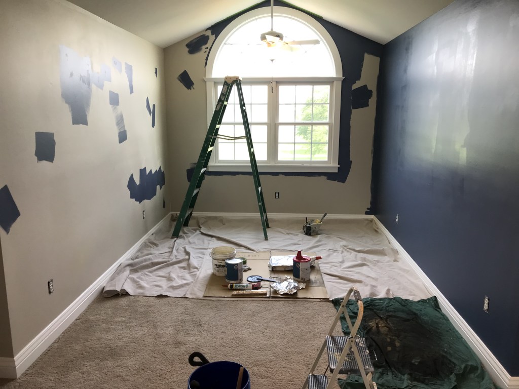 Upstairs room with large window that is part way through being painted blue. 